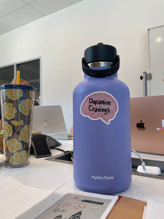Brain shaped pink sticker that says Dopamine Cravings in black font. Displayed on purple  water bottle.